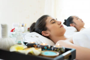 Woman lying relaxed on therapy plinth receiving gentle somatic therapy treatment, wearing comfortable clothing in a serene therapy room with natural lighting and calming decor, demonstrating professional bodywork session