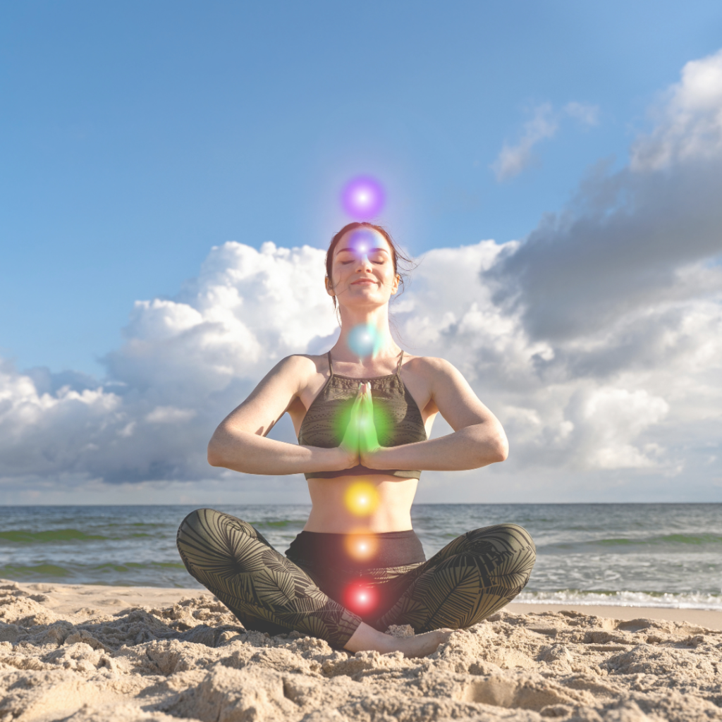 Woman meditating on a beach with visible chakra colors alignment for holistic wellness and energy balance