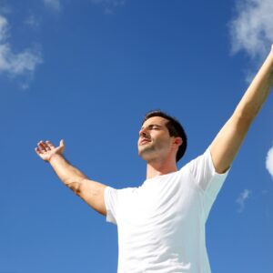 Man practicing somatic breathing with arms open under blue sky - anxiety relief techniques Ireland