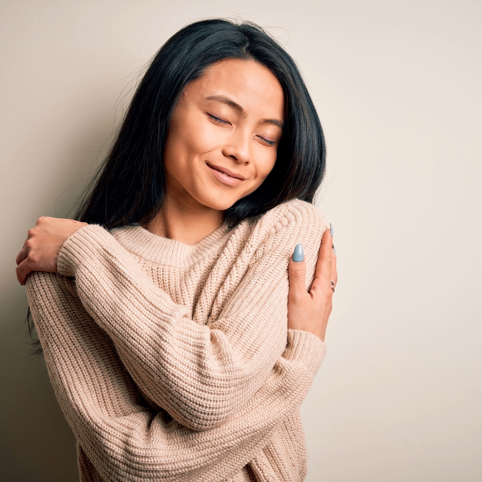 Woman with dark hair hugging herself with eyes closed, practising self-soothing and nervous system regulation through gentle self-embrace