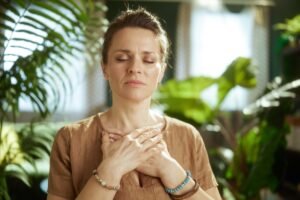 A woman with hands resting on her chest, eyes softly closed, in a calm moment of self-regulation — representing the heart of Integrative Somatic Therapy with Abi Beri.