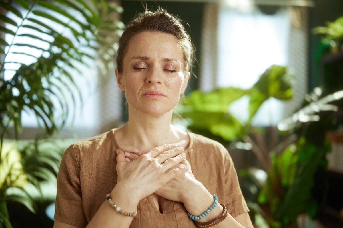 A woman with hands resting on her chest, eyes softly closed, in a calm moment of self-regulation — representing the heart of Integrative Somatic Therapy with Abi Beri.