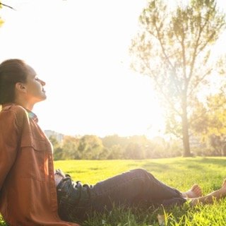 Woman sitting outdoors in a natural setting, looking out at the surroundings